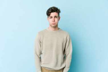 Mavi arka planda izole edilmiş genç beyaz adamın yanakları şişer, yorgun bir ifadesi vardır. Yüz ifadesi kavramı.