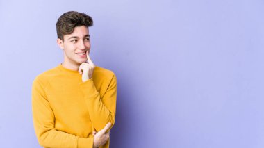 Mor arka planda izole edilmiş genç beyaz adam rahatlamış bir şeyin fotokopi odasına baktığını düşünüyor..