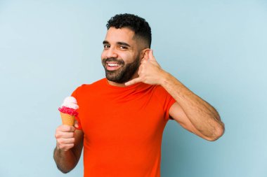 Dondurma tutan genç latin adam, parmaklarıyla bir cep telefonu hareketi gösteriyor..