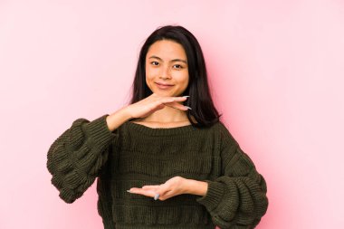 Pembe arka planda izole edilmiş genç Çinli bir kadın iki eliyle bir şey tutuyor, ürün sunumu..