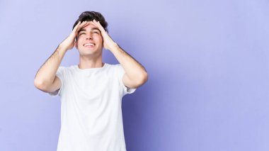 Mor arka planda izole edilmiş genç beyaz adam, mutlu bir şekilde ellerini başının üstünde tutarak gülüyor. Mutluluk kavramı.