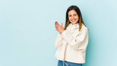 Mavi arka planda izole edilmiş genç bir kadın enerjik ve rahat hissediyor, ellerini ovuşturuyor..