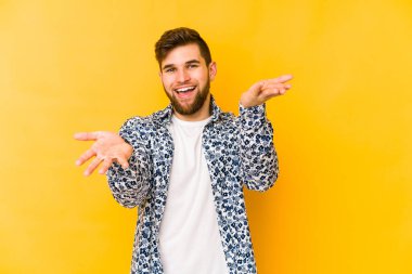 Sarı arka planda izole genç beyaz adam kollarıyla ölçek yapar, mutlu ve kendinden emin hisseder..