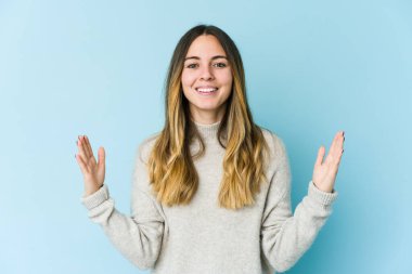 Kafkasyalı genç bir kadın mavi arka planda izole edilmiş. Elinde parmakları olan, gülümseyen ve kendinden emin bir şey var..