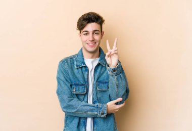 Beyazlı genç bir adam bej arka planda izole edilmiş. İki numarayı parmaklarıyla gösteriyor..