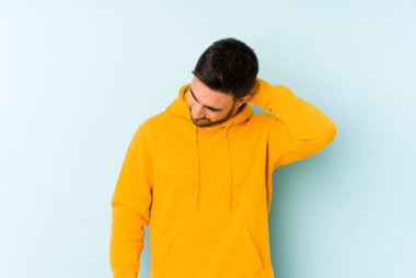 Kafkasyalı genç adam mavi arka planda izole edilmiş. Stres yüzünden boynu ağrıyor. Masaj yapıyor ve elle dokunuyor..