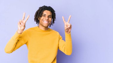 Rasta saç stili giyen genç siyah adam zafer işareti gösteriyor ve gülümsüyor..