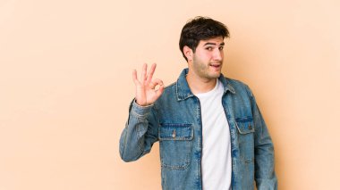 Bej arka planda izole edilmiş genç bir adam bir göz kırptı ve elleriyle iyi bir jest yaptı..