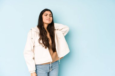 Mavi arka planda oturan genç Hintli kadın sabit yaşam tarzından dolayı boyun ağrısı çekiyor..