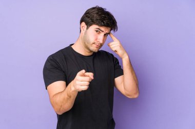Mor arka planda izole edilmiş genç bir adam şakağı parmağıyla işaret ediyor, düşünüyor ve bir göreve odaklanıyor..