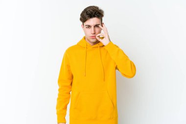 Beyaz arka planda izole edilmiş beyaz tenli genç bir adam parmakları dudaklarında bir sır saklıyor..