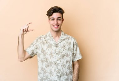 Beyaz tenli genç adam bej arka planda izole edilmiş. Elinde parmakları olan, gülümseyen ve kendinden emin bir şey var..