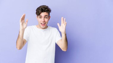Mor arka planda izole genç beyaz adam hoş bir sürpriz alıyor, heyecanlı ve el kaldırıyor..