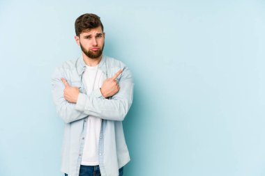 Mavi arka plan noktalarında izole genç beyaz adam, iki seçenek arasında seçim yapmaya çalışıyor.