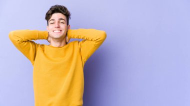 Mor arka planda izole olmuş genç beyaz bir adam kendini güvende hissediyor, elleri başının arkasında..