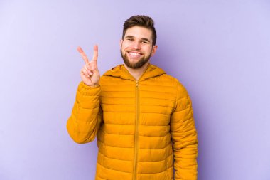 Mor arka planda izole edilmiş genç bir adam iki numarayı parmaklarıyla gösteriyor..