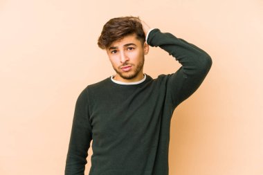 Bej bir arka planda izole edilmiş genç bir Arap adam yorgun ve uykulu bir şekilde ellerini başının üstünde tutuyor..