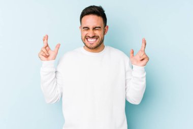 Kafkasyalı genç adam mavi arka planda izole edilmiş şans dilemek için şans diliyor.