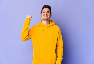 Mor arka planda izole edilmiş genç beyaz bir adam zaferi, tutkuyu ve coşkuyu kutluyor, mutlu bir ifade..