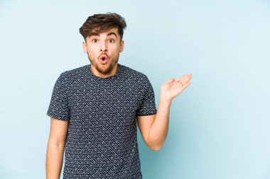 Mavi arka planda izole edilmiş genç bir Arap, avuç içi fotokopi alanını tutmaktan etkilenmiş..