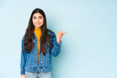 Mavi arka planda izole edilmiş genç Hintli kadın işaret parmağıyla fotokopi alanını işaret ederek şok oldu..