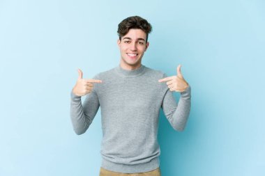 Kafkasyalı genç adam mavi arka planda izole edildi. Parmakları aşağıda, olumlu bir his var..