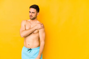Sarı arka planda mayosu olan genç, beyaz bir adam omuz ağrısı çeken beyaz bir adam..