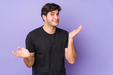 Mor arka planda izole edilmiş genç bir adam. Kafası karışmış ve omuz silkiyor. Kopya alanını tutmak için..