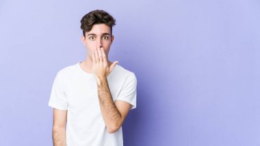 Mor arka planda izole edilmiş genç beyaz adam şok olmuş, ağzı ellerle kaplanmış, yeni bir şey keşfetmeye hevesli..
