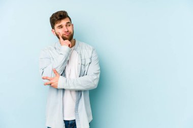 Kafkasyalı genç bir adam mavi arka planda izole edilmiş. Bir strateji planlıyor, bir iş yolu düşünüyor..