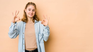 Beyaz tenli genç bir kadın bej arka planda izole edilmiş neşeli ve kendinden emin..