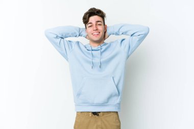 Beyaz arka planda izole olmuş genç beyaz bir adam kendini güvende hissediyor, elleri başının arkasında..