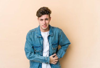 Beyazlı genç bir adam bej arka planda izole edilmiş karaciğer ağrısı, karın ağrısı var..