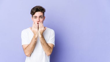 Mor arka planda izole edilmiş genç beyaz adam şok olmuş, ağzı ellerle kaplanmış, yeni bir şey keşfetmeye hevesli..