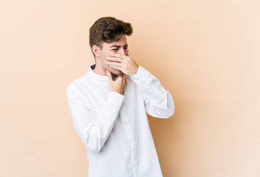 Beyazlı genç bir adam bej arka planda virüsten ya da enfeksiyondan boğaz ağrısı çekiyor..