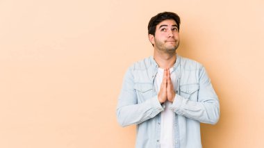 Bej arka planda izole edilmiş genç bir adam. El ele tutuşup, ağzının kenarında dua ediyor. Kendine güveniyor..