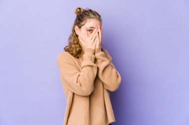 Mor arka planda genç beyaz bir kadın korkmuş ve gergin parmaklarıyla göz kırpıyor..
