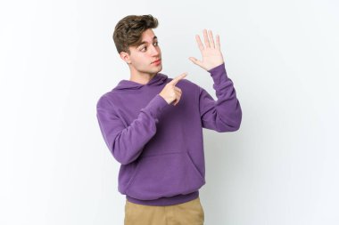 Beyaz arka planda izole edilmiş genç beyaz bir adam gülümseyerek beş numarayı parmaklarıyla gösteriyor..