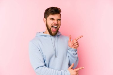 Pembe arka planda izole edilmiş genç beyaz adam işaret parmağıyla fotokopi alanını işaret ederek heyecan ve arzusunu ifade ediyor..
