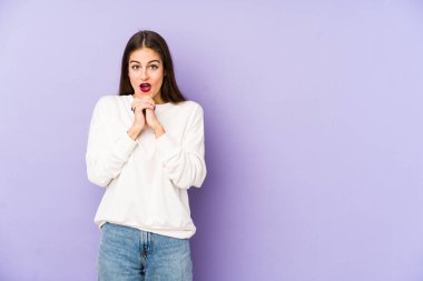 Mor arka planda izole edilmiş genç beyaz bir kadın şans için dua ediyor, hayrete düşüyor ve ağzını açıp önüne bakıyor..