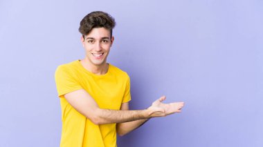 Mor arka planda izole edilmiş genç beyaz bir adam bir palmiyenin üzerinde bir kopya alanı tutuyor..