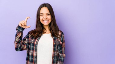 Genç, Latin kökenli bir kadın, kendini izole etmiş, parmaklarıyla küçük bir şey tutuyor, gülümsüyor ve kendinden emin..