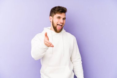 Mor arka planda izole edilmiş genç beyaz adam selamlama jesti olarak kameraya elini uzatıyor..