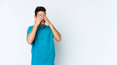 Beyaz arka planda izole edilmiş genç beyaz bir adam elleriyle gözlerini kapatmaktan korkuyor..