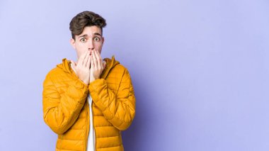 Mor arka planda izole edilmiş genç beyaz adam elleriyle ağzını kapatırken şok oldu..