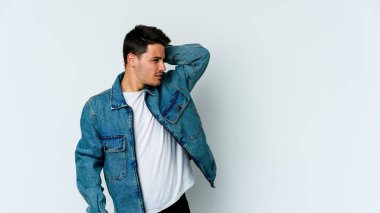 Beyaz arka planda izole edilmiş genç beyaz bir adam yorgun ve uykulu bir şekilde elini başının üstünde tutuyor..