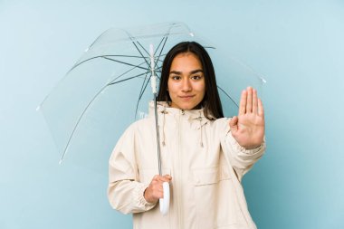 Genç Asyalı kadın elinde şemsiyeyle elini uzatarak dur işareti göstererek seni engelliyor..