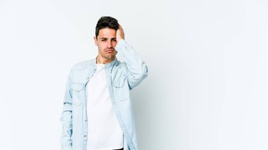 Beyaz arka planda izole edilmiş genç beyaz bir adam yorgun ve uykulu bir şekilde elini başının üstünde tutuyor..