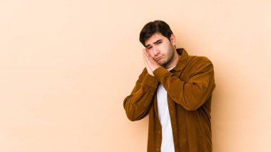 Bej arka planda izole edilmiş genç bir adam esniyor. Ağzı eliyle kapatan yorgun bir jest gösteriyor..