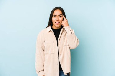 Mavi arka planda izole edilmiş genç bir kadın işaret parmağıyla bir hayal kırıklığı gösteriyor..